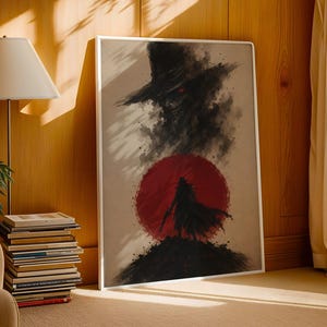 May include: A rectangular framed wall art print featuring a dark, ink-wash style illustration of a silhouetted figure in a wide-brimmed hat standing before a large, solid red circle. The artwork includes subtle text at the bottom center.