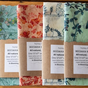 May include: Four beeswax food wraps with floral patterns in shades of blue, orange, and green. Each wrap is 13"x17" and wrapped with a brown paper label that reads "honey & BEESWAX". The wraps are hand crafted with organic beeswax.