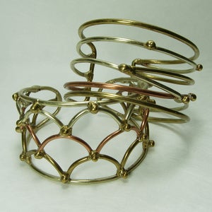 May include: A set of three silver and gold bangles with a copper accent. The bangles are stacked on top of each other and have a geometric design.