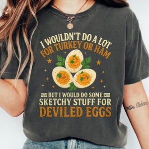 May include: Dark grey heather t-shirt with the text "I wouldn't do a lot for turkey or ham, but I would do some sketchy stuff for deviled eggs." The shirt features a graphic of three deviled eggs. The text "Dark Grey Heather" is at the bottom.