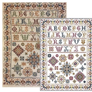 Op de afbeelding: Een kruissteek sampler met een witte achtergrond en een kleurrijke rand. De sampler bevat een volledig alfabet in een gestileerd lettertype, samen met verschillende geometrische ontwerpen en bloemmotieven. De sampler is ingelijst in een zwart frame.