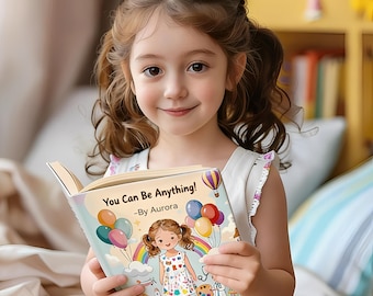 Peut inclure: Une jeune fille aux cheveux bruns et aux couettes sourit en tenant un livre pour enfants intitulé "You Can Be Anything!" par Aurora. La couverture du livre présente une illustration de dessin animé d'une fille, de ballons et d'un arc-en-ciel.