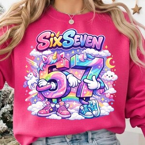 May include: A pink sweatshirt with the words "Six Seven" in a colorful, whimsical font. The number "67" is designed with unicorn-like features, rainbows, and clouds. The design is playful and suitable for a child's birthday.