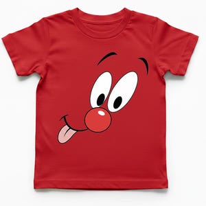 Può includere: T-shirt rosso con un disegno di un volto di cartone animato. Il volto ha grandi occhi bianchi, un naso rosso e una lingua che sporge. La grafica è centrata sulla maglietta, creando un design giocoso. La maglietta è in materiale morbido.