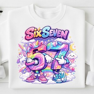May include: White sweatshirt featuring a colorful graphic with the words "Six Seven" above the numbers 6 and 7, designed as cartoon unicorns. The design includes rainbows, clouds, and stars, creating a whimsical and celebratory theme.