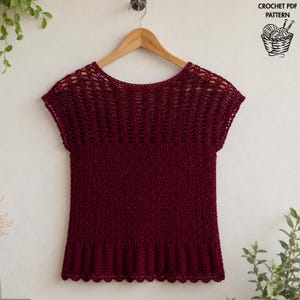 May include: A dark burgundy crochet top featuring a wide neckline, short sleeves, and a textured stitch pattern. The upper section has an openwork design, while the lower body is solid. Text in the upper right corner reads CROCHET PDF PATTERN.