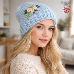 May include: A pale blue knitted beanie hat with embroidered flowers. The hat has a ribbed design and is decorated with cream and green floral embroidery. The text "Crochet pattern PDF" is visible in the upper right corner.