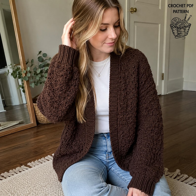 May include: A dark brown, long-sleeved, open-front cardigan with a textured, bobble-like stitch pattern, ribbed cuffs, and a ribbed collar. The garment is worn over a plain white t-shirt and light blue jeans. Text in the corner reads CROCHET PDF PATTERN.