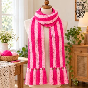 May include: A crochet scarf featuring vertical stripes in alternating shades of hot pink and light pink. The scarf is wrapped around a mannequin neck and finished with long, matching pink yarn tassels at both ends. Text reads CROCHET PDF PATTERN.