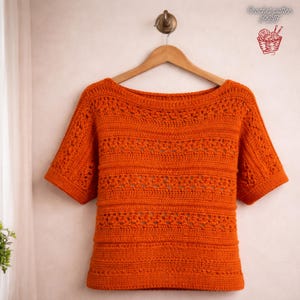 May include: A white ceramic mug with a black handle and the text "But First, Coffee" in a bold, black font. The mug is set against a blurred background, suggesting a cosy setting.