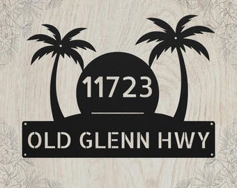 May include: A black metal address sign featuring two palm trees flanking a central circular sun shape. The number 11723 is displayed in the center, and the text OLD GLENN HWY is cut out in a rectangular bar at the bottom of the design.