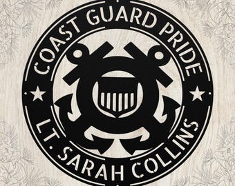 May include: Black metal Coast Guard Pride sign with anchors, a shield, and stars. The text reads "Coast Guard Pride" and "Lt. Sarah Collins" in a circular design. The sign is on a light wood-grain background.
