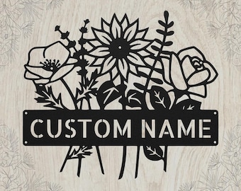May include: A black metal wall sign featuring a laser-cut floral arrangement with a sunflower, a rose, and other botanical elements. A horizontal rectangular bar is integrated into the design, displaying the stencil-style text CUSTOM NAME.