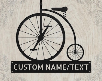 May include: A black metal wall sign featuring a silhouette of a penny-farthing bicycle with a large front wheel and a small rear wheel. Below the bicycle is a rectangular plate with the stencil-style text CUSTOM NAME/TEXT.