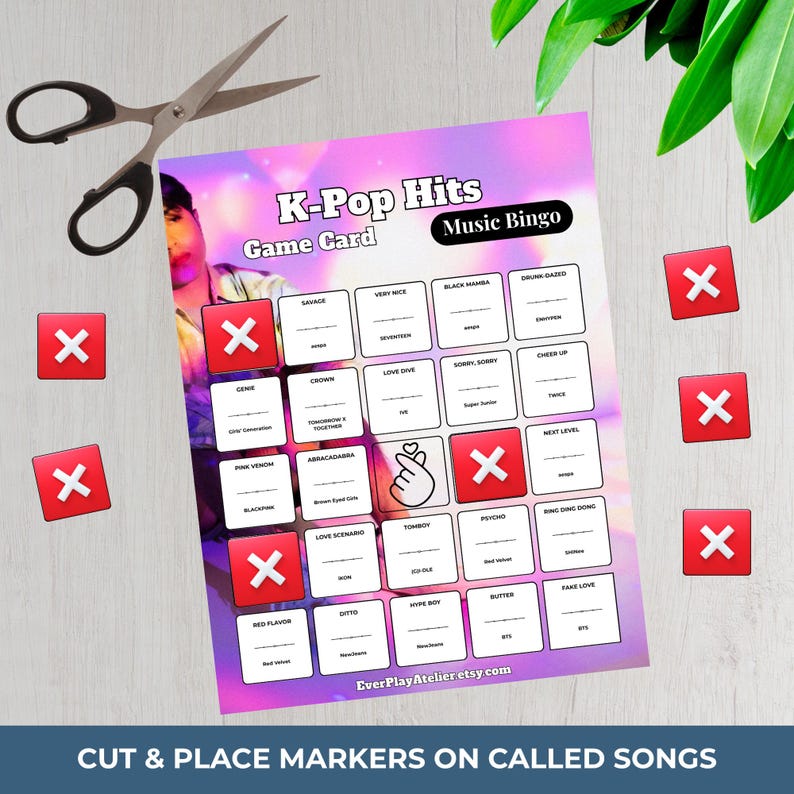 Pu&ograve; includere: Una scheda di gioco K-Pop Hits Music Bingo con pennarelli rossi e forbici. La scheda presenta titoli di canzoni e il testo "Cut & Place Markers on Called Songs". Lo sfondo &egrave; una sfumatura di viola chiaro e rosa.