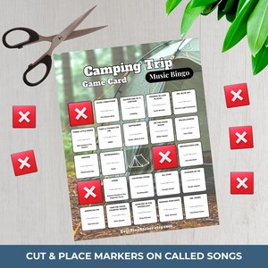 Puede incluir: Una tarjeta de juego de Bingo musical Camping Trip con t&iacute;tulos de canciones, marcadores X rojos y tijeras. La tarjeta de juego presenta un gr&aacute;fico de tienda de campa&ntilde;a y el texto "Corta y coloca marcadores en las canciones llamadas."