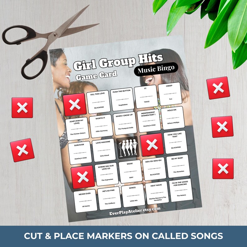May include: A Girl Group Hits Music Bingo game card with song titles and red X markers. The card features a photo of women and the text "Cut & Place Markers on Called Songs". A pair of scissors is on the left.