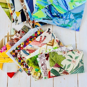 May include: A collection of assorted envelopes featuring diverse printed patterns including abstract blue and green brushstrokes, geometric shapes, floral motifs, and illustrated animal designs, all arranged in a layered, overlapping fan formation.