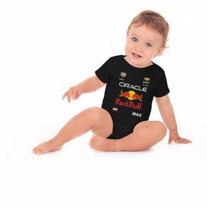 Puede incluir: Body de beb&eacute; negro con el logo de Red Bull Racing, las palabras "ORACLE" y "MAX" impresas en la parte delantera. El body tiene mangas cortas y cuello redondo. El logo de Red Bull es un toro rojo frente a un c&iacute;rculo amarillo.