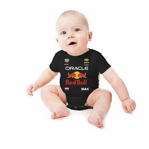 Puede incluir: Body de beb&eacute; negro con el logo de Red Bull Racing, incluyendo el texto Oracle y Max. El body tiene mangas cortas y cuello redondo. El dise&ntilde;o incluye el logo de Red Bull con un sol amarillo y dos toros rojos.