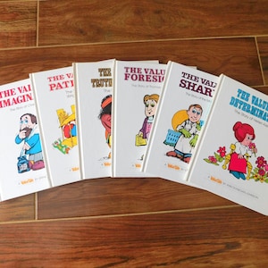 May include: A collection of six vintage children's books with white covers and colorful illustrations. Titles include "The Value of Imagination," "The Value of Patience," and "The Value of Determination." The books are arranged in a fan shape on a wooden surface.