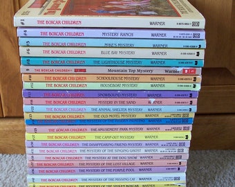 Puede incluir: Una pila de 25 libros de bolsillo con cubiertas de colores. Los libros son todos parte de la serie "The Boxcar Children". Los libros están ordenados del 1 al 25. Los títulos de los libros son visibles en los lomos. Los libros están todos publicados por Warner.