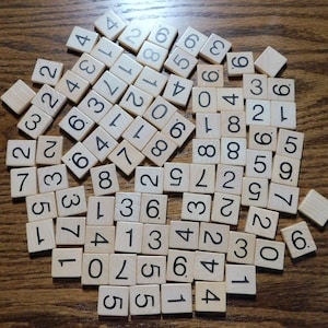 May include: A collection of wooden tiles with numbers printed on them. The tiles are arranged in a circular pattern on a wooden surface.