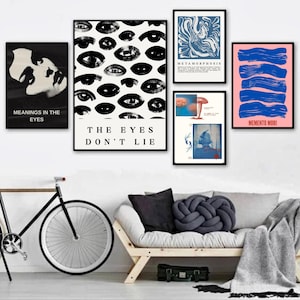 Puede incluir: Una colección de impresiones artísticas enmarcadas exhibidas en una pared blanca. Las impresiones presentan varios diseños abstractos, incluyendo ojos, patrones arremolinados y texto. La paleta de colores incluye negro, blanco, azul y rosa. Una bicicleta y un sofá están en primer plano.