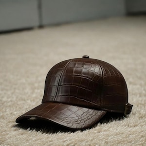 May include: A brown baseball cap with a textured, crocodile-like pattern. The cap features a curved peak and an adjustable strap. The cap is made of a leather-like material.