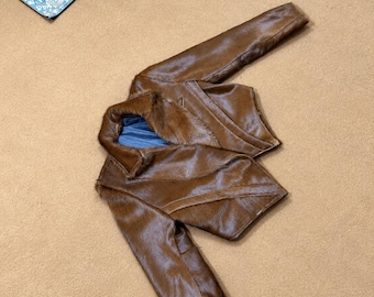 Könnte beinhalten: Eine braune, kurz geschnittene Jacke mit texturierter Felloptik, langen Ärmeln, einem breiten Kragen und einem blauen Innenfutter. Das Kleidungsstück hat ein strukturiertes Design mit diagonalen Nahtdetails auf den Vorderteilen.