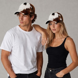 May include: Two people wearing matching baseball caps. The caps have a brown, white, and black cowhide pattern on the crown and a black brim. One person is wearing a white t-shirt, and the other is wearing a black tank top.