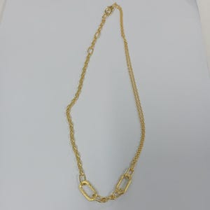 Op de afbeelding: Een goudkleurige ketting met een kettingontwerp. De ketting heeft een combinatie van een touwketting en een ketting met rechthoekige schakels. De ketting wordt op een witte achtergrond gepresenteerd.