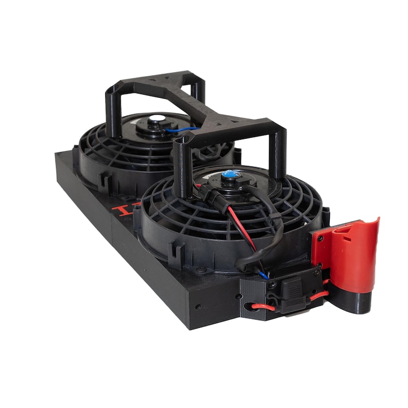 May include: Dual electric radiator fan assembly. The assembly features two black fans with protective grilles, mounted on a black base. A red component is attached to the side, with wiring visible. The fans are connected by a black support structure.
