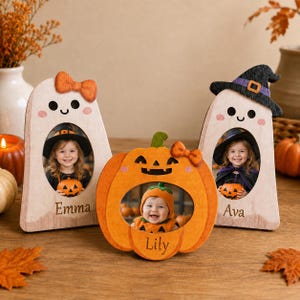 Può includere: Tre cornici portafoto in legno a forma di due fantasmi e una zucca. Il fantasma a sinistra ha un fiocco arancione, quello a destra indossa un cappello da strega nero e la zucca centrale ha un fiocco arancione. Ogni cornice mostra una foto e un nome.