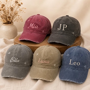 Può includere: Cinque cappellini da baseball vintage in vari colori: bordeaux, antracite, kaki, blu denim e grigio. Ogni cappellino presenta un nome diverso ricamato in un colore a contrasto: Mia, JP, Ella, Luna e Leo. I cappellini hanno un aspetto vintage usurato.