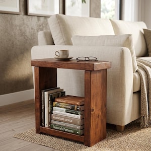 May include: A rectangular dark brown wooden side table with a flat top surface and an open lower shelf. The shelf contains a stack of books with visible titles including Meditations, The Overstory, Furniture Design, and Nature's Patterns.