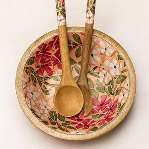 Peut inclure: Un saladier en bois avec un motif floral en mosaïque dans les tons de rouge, blanc et vert. Deux cuillères en bois avec des motifs floraux reposent à l'intérieur. Le bol a un bord doré.