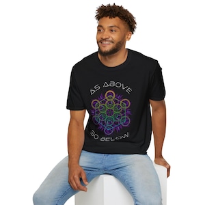 May include: Black t-shirt with the text "AS ABOVE SO BELOW" in white. The shirt features a geometric design with purple, green, and gold accents. The model is wearing blue jeans.