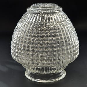 May include: Clear glass lampshade with a textured, bubble-like pattern. The shade has a rounded, bell-like shape with a decorative top and a flared base. The glass is transparent, allowing light to pass through, and is suitable for a vintage or retro aesthetic.