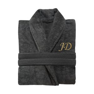Puede incluir: Bata de ba&ntilde;o de rizo gris oscuro con cuello chal y cintur&oacute;n a juego. La bata presenta las iniciales doradas "JD" bordadas en el pecho. La bata est&aacute; cuidadosamente doblada, mostrando su textura afelpada y dise&ntilde;o.