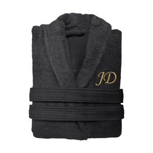 Puede incluir: Bata de rizo negra con cuello chal y dos cinturones en la cintura. La bata presenta las iniciales doradas "JD" bordadas en el pecho. La bata est&aacute; doblada y lista para usar.