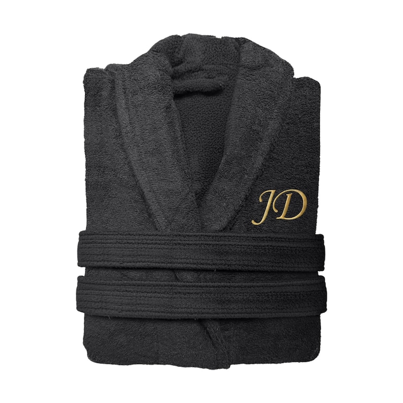 Puede incluir: Bata de rizo negra con cuello chal y dos cinturones en la cintura. La bata presenta las iniciales doradas "JD" bordadas en el pecho. La bata est&aacute; doblada y lista para usar.