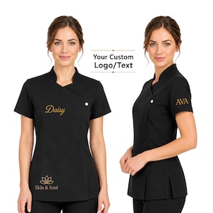 Op de afbeelding: Zwart spa-uniform met korte mouwen en een opstaande kraag. Het uniform heeft een wikkelvoorkant met een enkele knoopsluiting. De tekst "Daisy" en een lotusbloemlogo met "Skin & Soul" zijn goudkleurig geborduurd. De tekst "Your Custom Logo/Text" is ook zichtbaar.