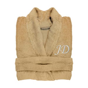 Puede incluir: Una bata de felpa plegada, de color beige, con cuello chal y cintur&oacute;n. La bata presenta las iniciales "JD" bordadas en blanco en el pecho. Fabricada con un material suave y absorbente, ideal para despu&eacute;s de la ducha.