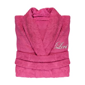 Puede incluir: Una bata de felpa rosa vibrante con cuello chal y cintur&oacute;n. La palabra "Levi" est&aacute; bordada en cursiva en el pecho. La bata est&aacute; doblada, mostrando su textura afelpada y dise&ntilde;o.