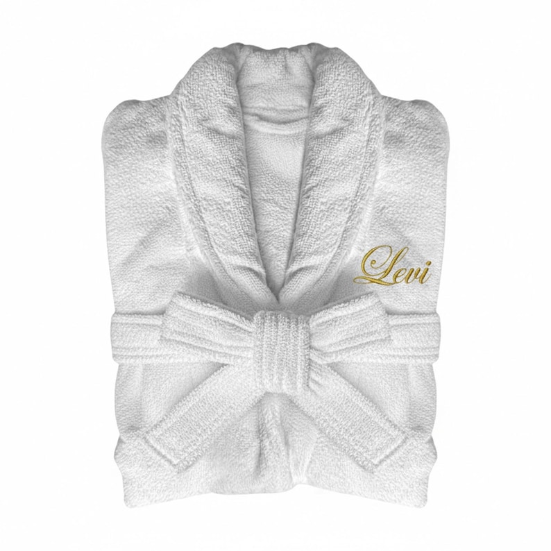 Puede incluir: Bata de ba&ntilde;o blanca de rizo con cuello chal y cintur&oacute;n adjunto. La palabra "Levi" est&aacute; bordada en oro en el pecho. La bata est&aacute; doblada cuidadosamente, mostrando la textura de la tela.