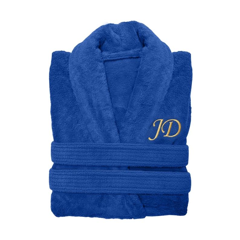 Puede incluir: Bata de rizo azul real con cuello chal y cintur&oacute;n a juego. La bata presenta las iniciales "JD" bordadas en hilo dorado en el pecho. La bata est&aacute; doblada cuidadosamente, mostrando su textura afelpada.