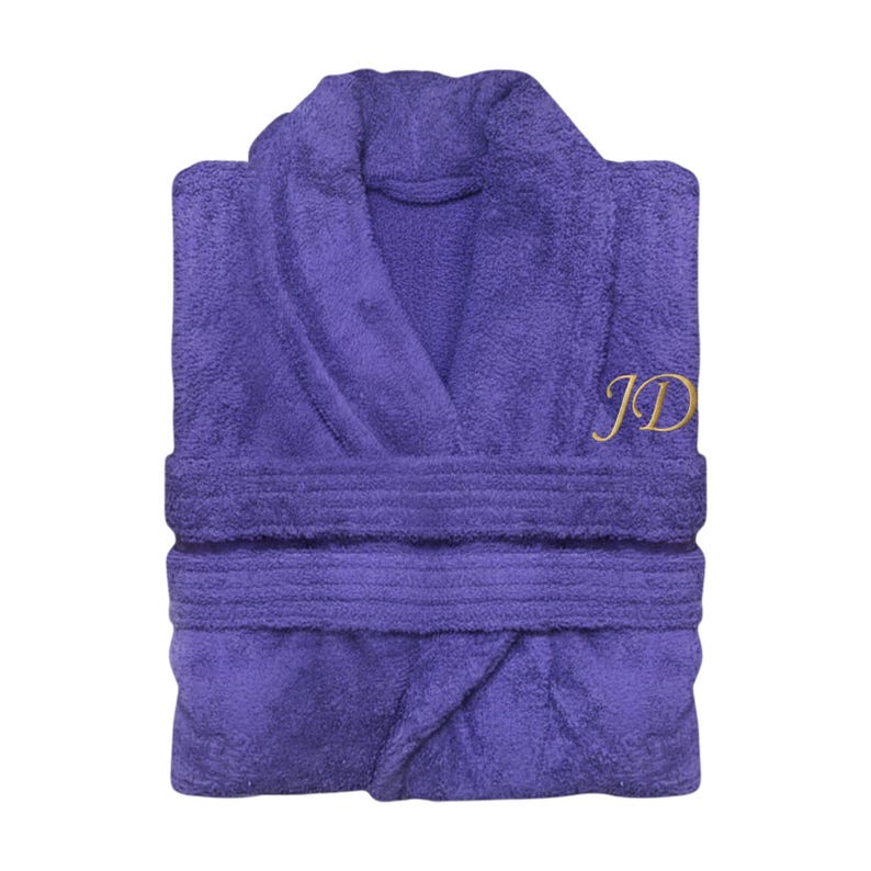 Puede incluir: Una bata morada doblada, con cuello chal y cintur&oacute;n. La bata presenta las iniciales "JD" bordadas en hilo dorado en el pecho. El material de rizo es visible, lo que sugiere comodidad y absorci&oacute;n.