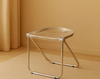 Pode incluir: Uma cadeira lateral de acrílico transparente e metal. O assento é um retângulo arredondado transparente. As pernas são de metal prateado. A cadeira está sobre um tapete bege, com uma parede e uma cortina bege ao fundo.