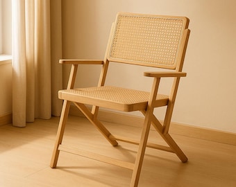 Pode incluir: Uma cadeira dobrável de madeira clara com encosto e assento em rattan tecido. A cadeira tem apoios de braços e está posicionada em frente a uma janela com cortinas bege. A cadeira é de madeira clara.
